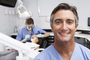 Portrait Of solo owner dentist With Dentist Examining Patient In Background needing private dental practice services